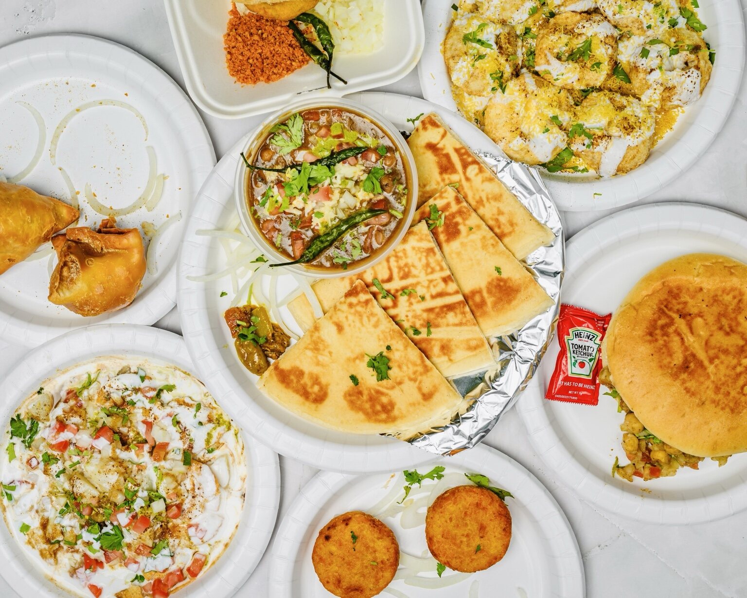 A full spread of Chaat on Wheels dishes including chaat, sandwiches, samosas and vada pav