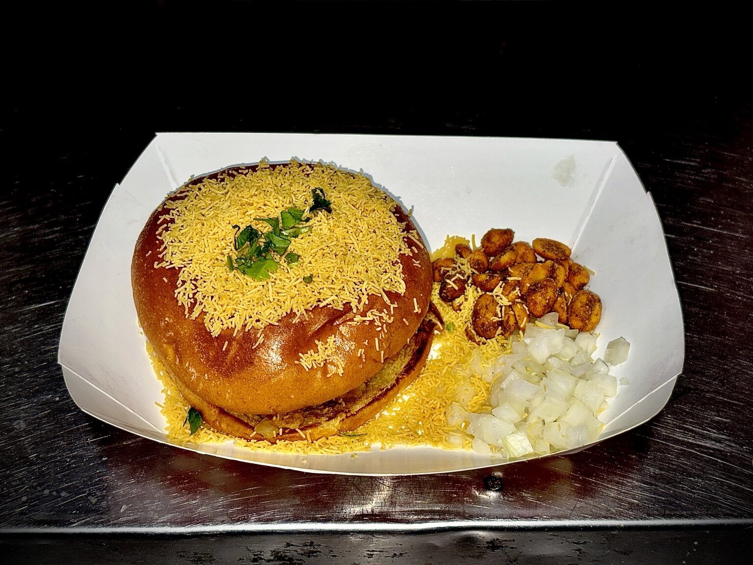 Dabeli topped with sev and served with peanuts and onions
