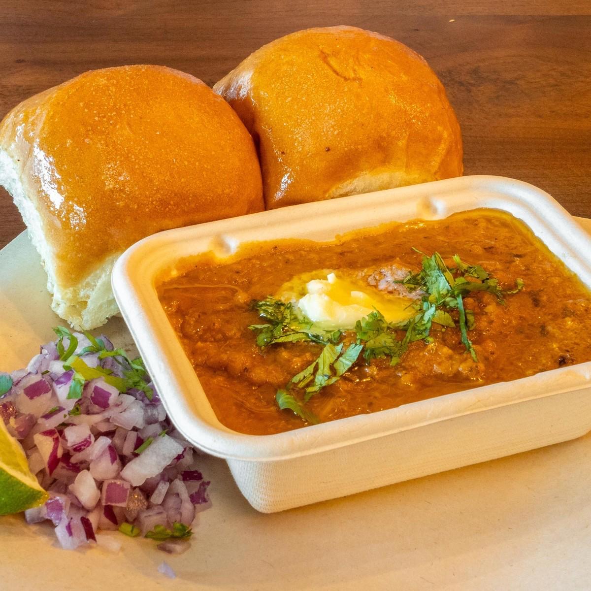 Pav bhaji served with buttered bread rolls, onions and lime